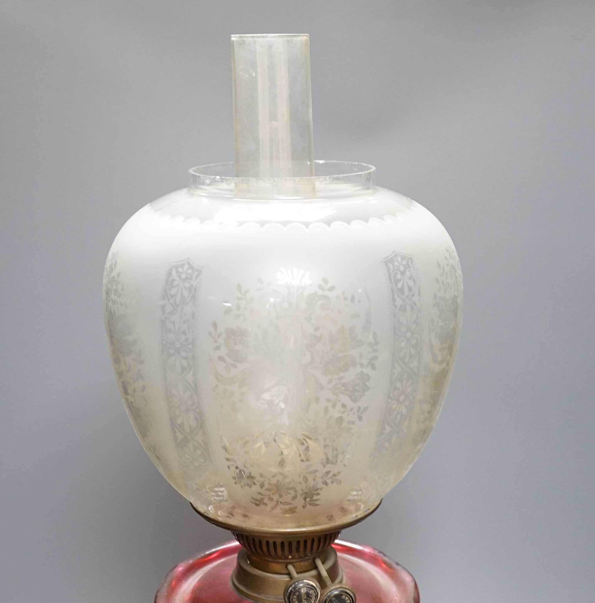 A brass and cranberry glass oil lamp with shade and chimney, total height 66cm